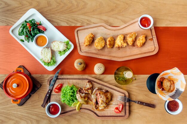 Gebratene Hühnerteile und Nuggets werden auf einem Holzbrett mit Salat, Tomaten, Öl und Gewürzen serviert