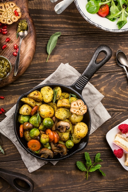 Gebratene Kartoffeln mit Gemüse und Kräutern auf hölzernem Hintergrund.