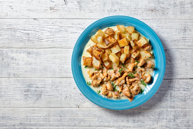 Gebratene Kartoffelstücke serviert mit Pfifferlingsauce auf blauem Teller, horizontale Ansicht von oben, flach, freier Raum