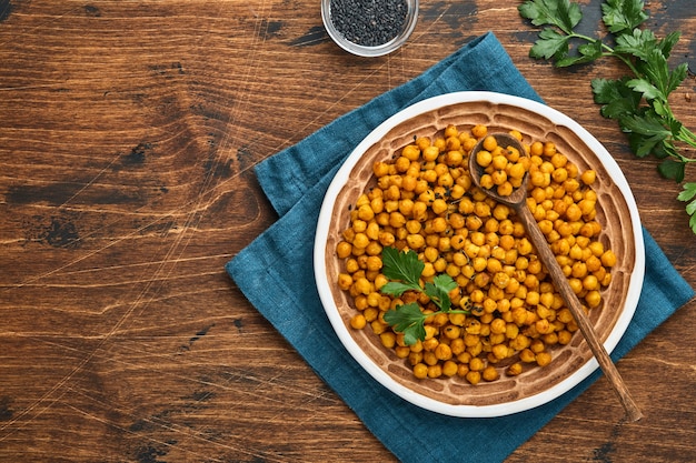 Gebratene Kichererbsen mit Kurkuma in Keramikplatte auf einem alten Holztischhintergrund. Geröstete würzige Kichererbsen oder indisches Chana oder Chole, beliebtes Snackrezept. Ansicht von oben.