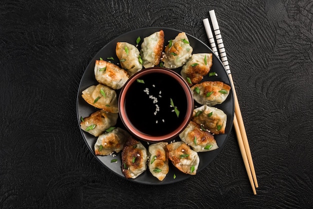 Foto gebratene knödel mit schweinefleisch und kräutern auf einem schwarzen runden teller mit sojasauce in der mitte auf dunklem hintergrund mit stäbchen koreanisches essen draufsicht mit copypaste für den text