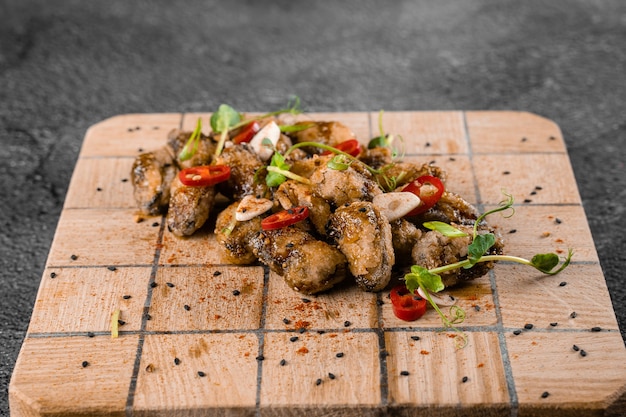 Gebratene Muscheln mit Chili, Knoblauch, Sesam, Kräutern, auf quadratischem Holzbrett auf grauer Oberfläche.