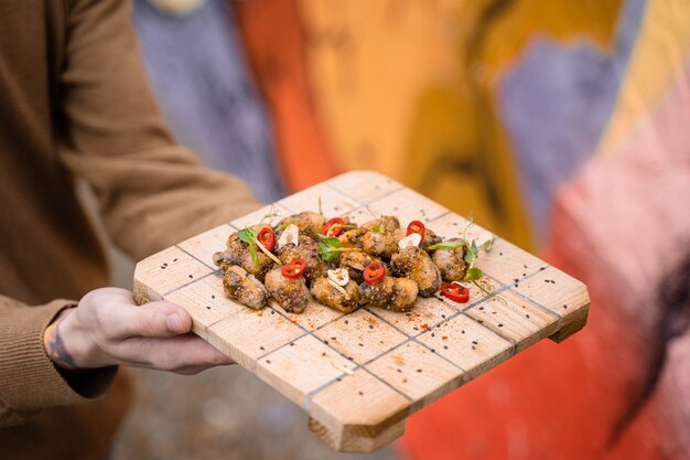 Gebratene Muscheln mit Chili, Knoblauch, Sesam, Kräutern auf quadratischem Holzbrett. Servieren Sie das Gericht vom Kellner.