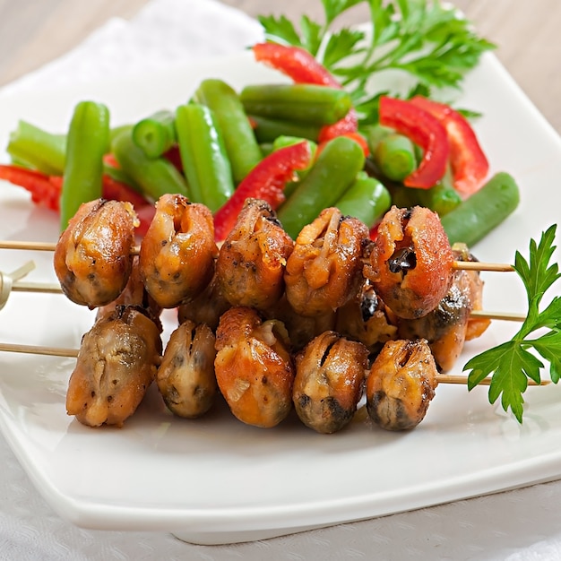 Gebratene Muscheln mit Zwiebeln am Spieß, garniert mit grünen Bohnen und Paprika