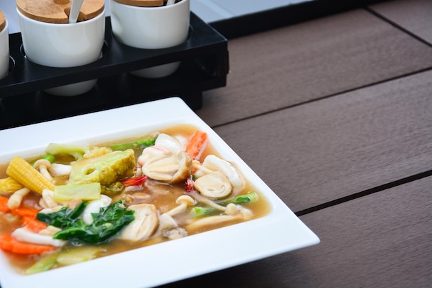 Foto gebratene nudeln mit meeresfrüchten, pilzen und gemüse in dicker soßensauce auf einem holztisch