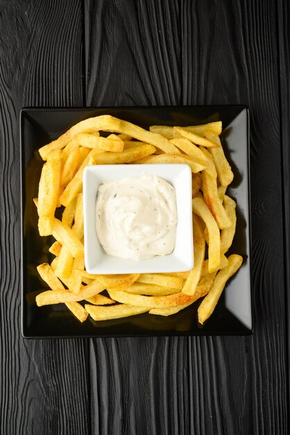 Gebratene Pommes Frites auf einem Teller mit Sauce auf schwarzem Holzhintergrund