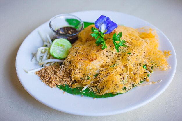 Gebratene Reisnudeln mit Garnelen in einer dünnen Omelettverpackung werden mit frischen Bohnensprossen und Zitrone serviert. Es ist ein thailändischer Streetfood-Stil.