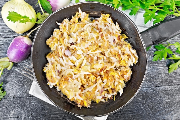 Gebratene Rüben mit Zwiebeln in einer Pfanne auf einem Handtuch auf Holzbretthintergrund von oben