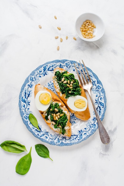 Gebratene Sandwiches mit Spinat, Ei und Pinienkernen auf heller Oberfläche. Leckeres gesundes Frühstück oder Snack. Draufsicht.