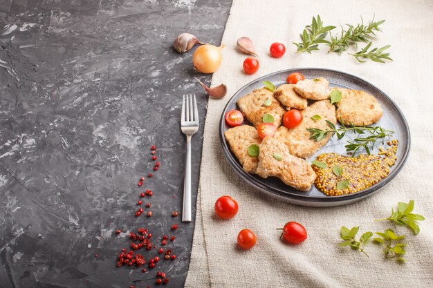 Gebratene Schweinekoteletts mit Tomaten und Kräutern auf einer grauen keramischen Platte auf einem schwarzen konkreten Hintergrund. Seitenansicht, Kopie, Raum.