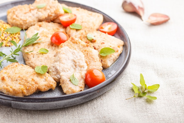 Gebratene Schweinekoteletts mit Tomaten und Kräutern auf einer grauen keramischen Platte. Seitenansicht