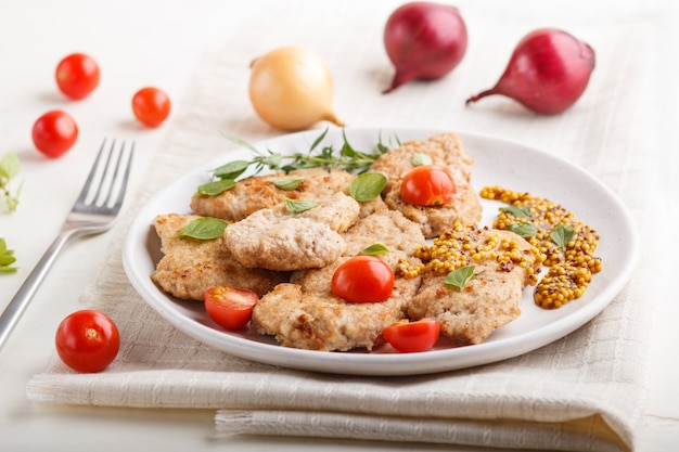 Gebratene Schweinekoteletts mit Tomaten und Kräutern auf einer weißen keramischen Platte auf einem weißen hölzernen Hintergrund. Seitenansicht, Nahaufnahme.