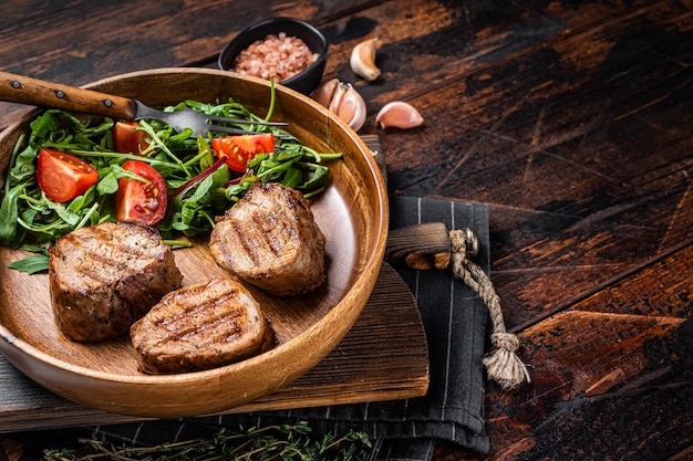 Gebratene Schweinemedaillonsteaks vom Filetfilet mit Gemüsesalat in Holzplatte Holzhintergrund Draufsicht Kopierbereich