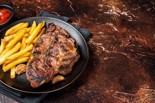 Gebratene Schweinesteaks aus Nackenfleisch in Platte mit Kartoffelchips Dunkler Hintergrund Draufsicht Kopierbereich