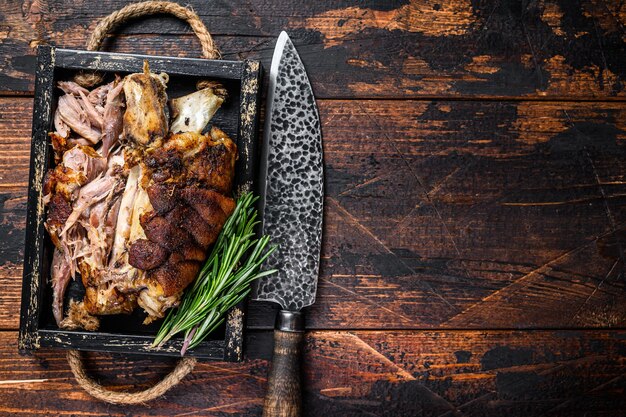 Gebratene Schweinshaxe Eisbein Fleisch in einem Holztablett mit Messer. Dunkler hölzerner Hintergrund. Ansicht von oben. Platz kopieren.