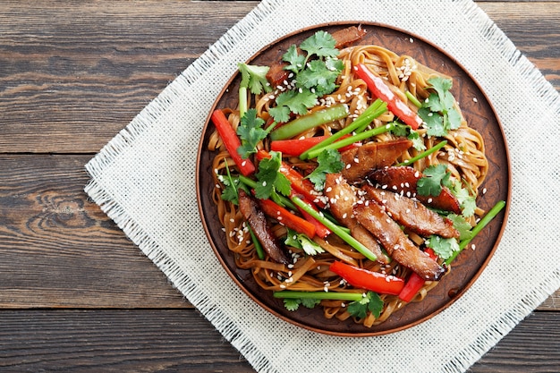 Foto gebratene soba-nudeln mit putenfleisch, kräutern und paprika auf einem keramikteller. draufsicht