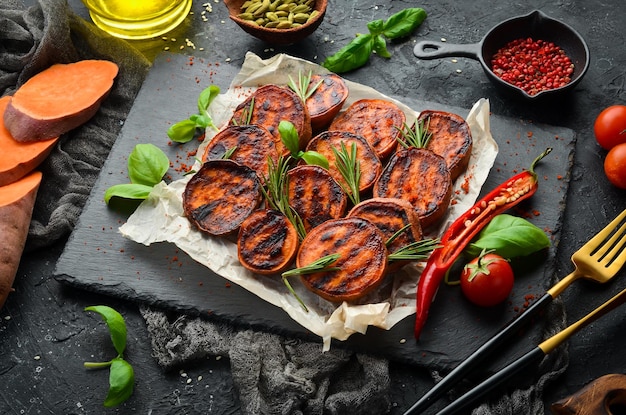 Gebratene Süßkartoffeln mit Rosmarinpaprika und Chilischoten auf einer schwarzen Steinplatte Draufsicht Freier Platz für Ihren Text