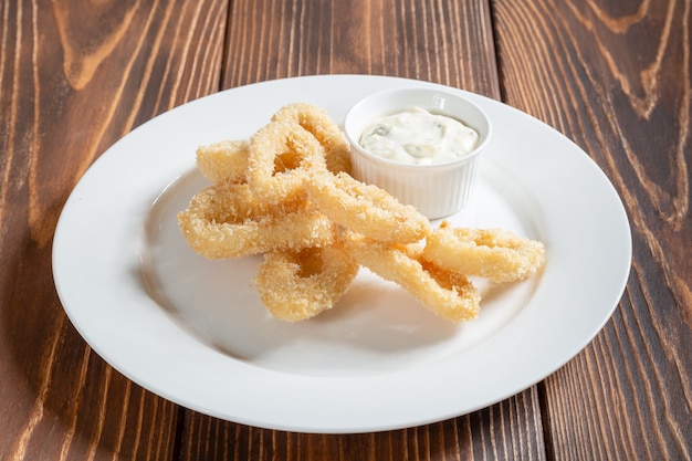 Gebratene Tintenfischringe mit Topf Tartarsauce auf Holztisch