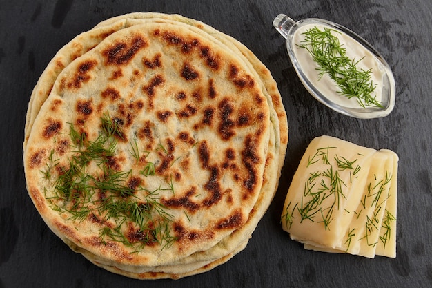 Gebratene Tortillas mit Käse und Kräutern und Joghurtsauce auf einem weißen Teller auf einem dunklen Steintisch