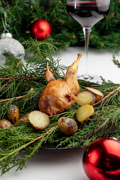 Gebratene Wachteln auf einem mit grünen Zweigen dekorierten Teller mit einem Glas Rotwein auf weißem Weihnachtshintergrund