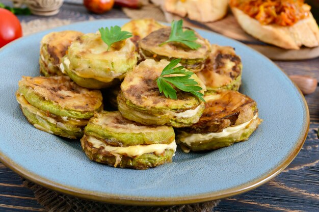 Gebratene Zucchinistücke mit Mayonnaise auf einem Keramikteller auf einem Holztisch.