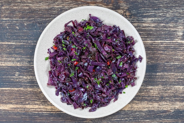 Gebratener Blaukohl mit Zwiebelapfel und Knoblauch in der Platte auf Draufsichtnahaufnahme des Holztischs