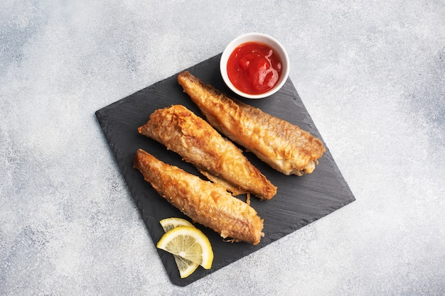 Gebratener Fisch Seehecht Pollock mit Tomatensauce und frischen Zitronenscheiben. Konzept essen fettiges Fast Food. Grauer konkreter Hintergrundkopierraum.