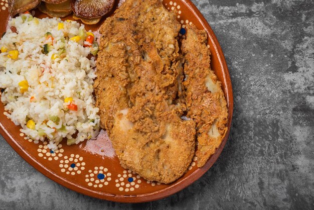 Gebratener Fisch und Reis in einer Lehmschüssel auf einem Holztisch