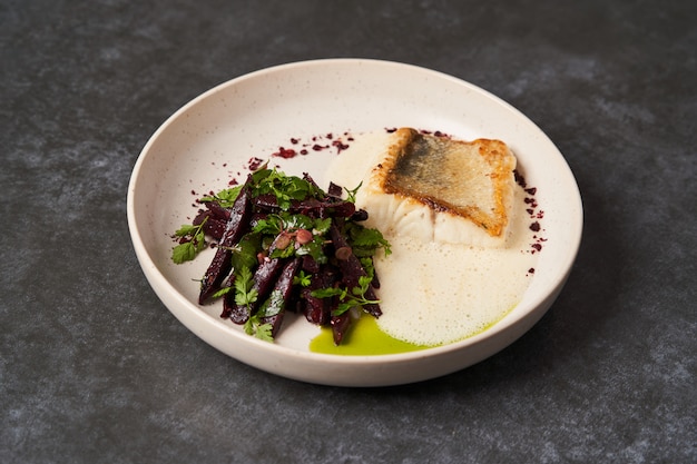 Gebratener Fischbarsch mit Gemüse auf einem weißen Tisch auf grauem Tisch