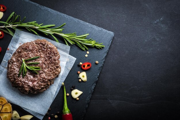 Gebratener frischer großer Rindfleischburger mit Kräutern und Knoblauch auf schwarzem Schiefer, Draufsicht, Platz für Text