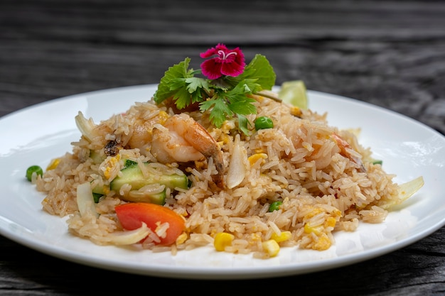 Gebratener Reis mit Garnelen und Gemüse in einem weißen Teller auf einem alten Holztisch, Nahaufnahme. Thailändisches Essen, thailändische Küche. Gebratener Reis mit Meeresfrüchten im Restaurant