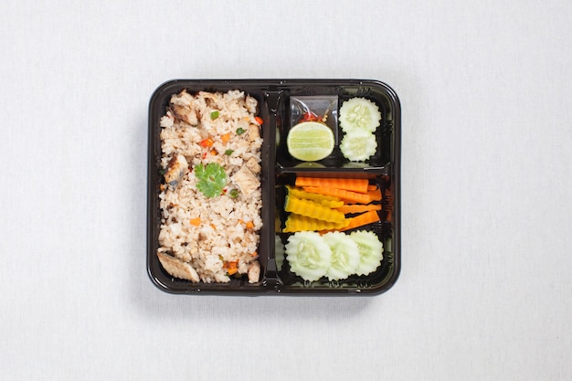 Gebratener reis mit gebratenem thunfisch in schwarzer plastikbox, weiße tischdecke, lebensmittelbox, thailändisches essen.