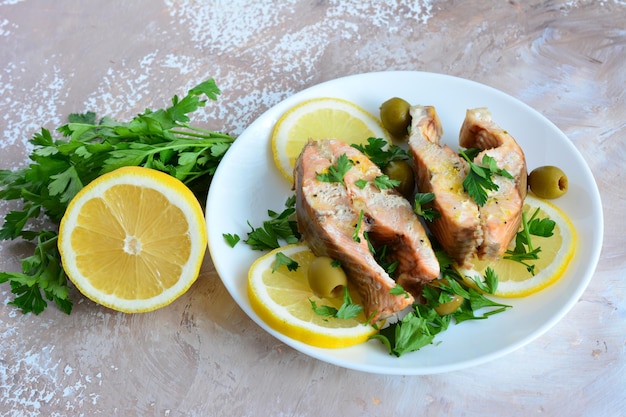 Gebratener rosa Lachs mit Petersilie und Zitronenscheiben auf weißem Teller, Nahaufnahme