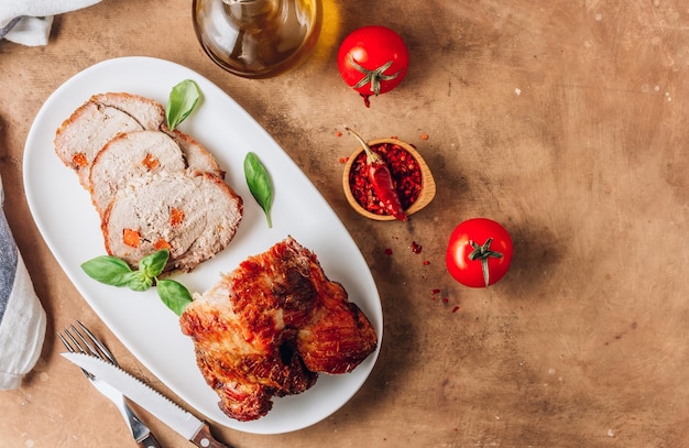 Gebratener Schweineschinken in Scheiben auf einem weißen Teller auf beigem, rustikalem Hintergrund, Draufsicht