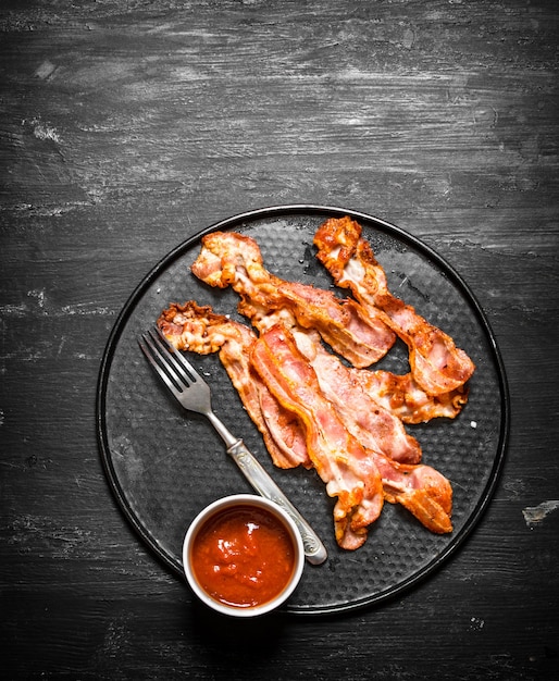 Gebratener Speck und Tomatensauce auf einem schwarzen hölzernen Hintergrund