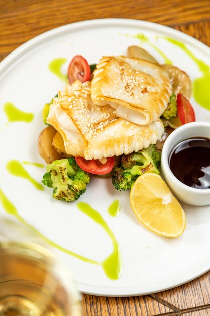 Gebratener Tintenfisch mit Gemüse, Kartoffeln und Zitrone. Serviert mit einem Glas Wein