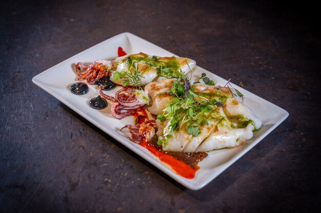 Gebratener Tintenfisch mit Sauce auf schwarzem Hintergrund, auf einem weißen Teller