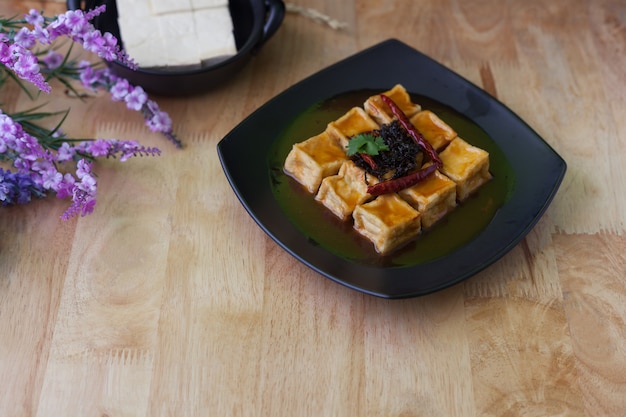 Gebratener Tofu im schwarzen Teller auf hölzernem Hintergrund