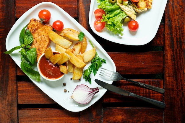 Gebratener Tofu mit Gewürzkartoffeln mit frischen Tomaten auf einem weißen Teller aus Holz