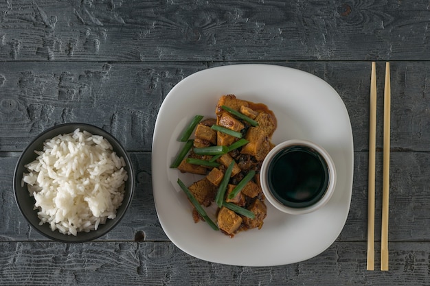 Gebratener Tofu mit Reis und Sojasauce auf einem weißen Teller. Flach liegen. Vegetarisches asiatisches Gericht.