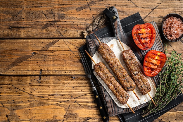 Gebratener türkischer Adana Schaschlik auf einem Brett mit gegrillter Tomate. Hölzerner Hintergrund. Ansicht von oben. Platz kopieren.