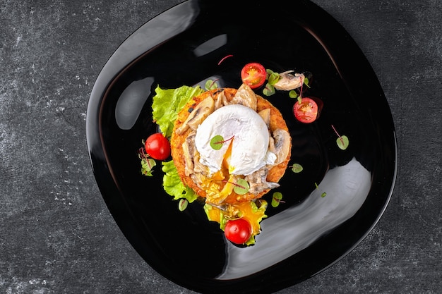 Gebratenes Beefsteak mit Pilzen, pochiertem Ei und Tomaten auf einem schwarzen Teller