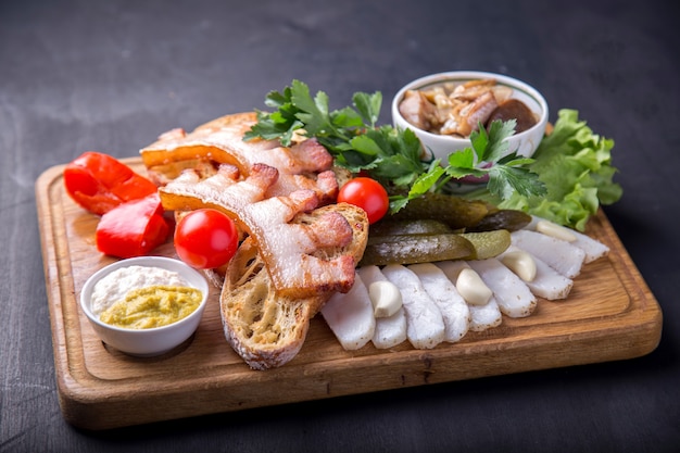 Gebratenes Bruststück mit gebratenen Brotstücken, geschnittenem Schmalz, frischen Tomaten und marinierten Pilzen. Leckere Vorspeise auf Holzbrett