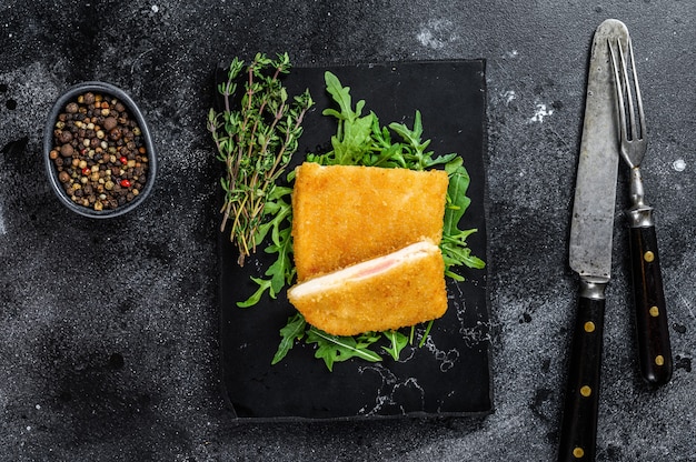 Gebratenes Cordon Bleu Hähnchenschnitzel mit Schinken und Käse. Schwarzer Hintergrund. Ansicht von oben.