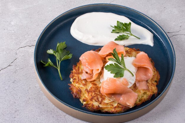 Gebratenes Draniki mit rot gesalzenem Fisch und pochiertem Ei. Ein mit Kräutern und Sauerrahm dekoriertes Gericht