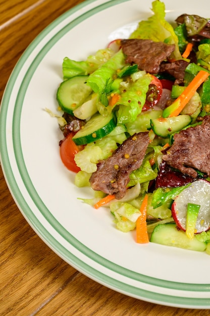 Gebratenes Fleisch mit Gemüse. Salat mit Fleisch, Tomaten, Paprika, Gurken und Salat auf Holzhintergrund