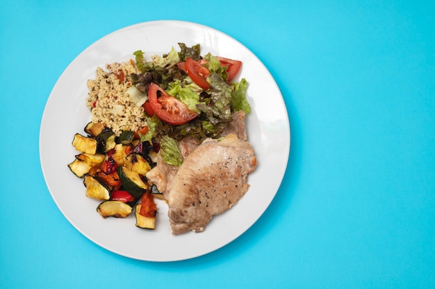 Gebratenes Fleisch mit Salat und Gemüse auf weißer Platte auf Blau