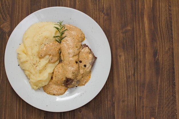 Gebratenes Fleisch mit Soße und Kartoffelpüree auf weißer Platte auf braunem Holz