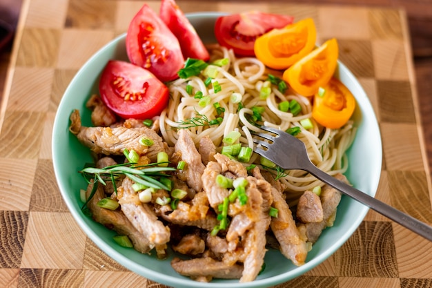 Gebratenes Fleisch und Spaghetti auf einem Teller auf einem hölzernen Hintergrund mit Tomaten und Kräutern.