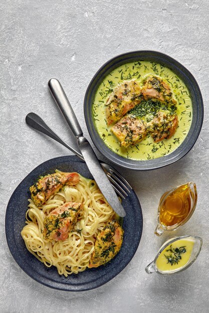 Gebratenes Geflügelhähnchen, gebacken mit Knoblauch und Kräutern in Milchcreme und Nudeln. Gebratenes Hähnchen mit Spaghetti auf dunklen Tellern auf einem grauen Betontisch